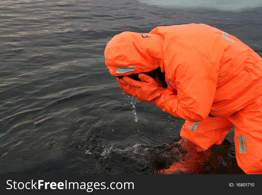 Human being in the water in a red rescue suit. The human being wash his face with cold water. Maybe his eyes are burning because of rays, heat or fire. Human being in the water in a red rescue suit. The human being wash his face with cold water. Maybe his eyes are burning because of rays, heat or fire.