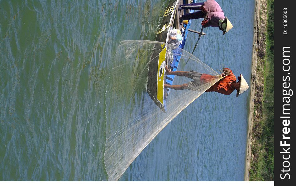 Couple fishing with a net into the boat. The woman stabilizes the boat with his oar while the man goes back in net. Couple fishing with a net into the boat. The woman stabilizes the boat with his oar while the man goes back in net.