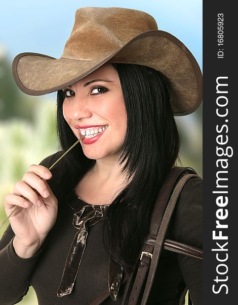 A smiling cowgirl country girl smiling and chewing on a piece of lucerne hay against a mountain landscape. A smiling cowgirl country girl smiling and chewing on a piece of lucerne hay against a mountain landscape.