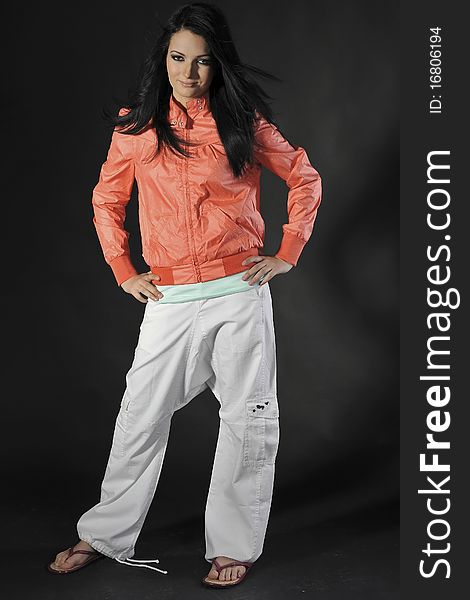 Sexy young slim brunette wearing orange jacket, white ducks and flip-flops (Isolated on the black background)