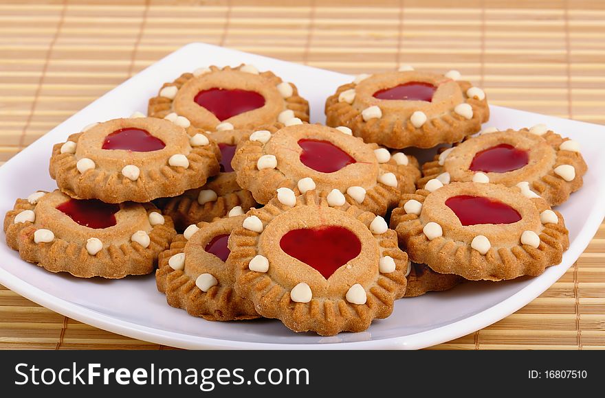 Cookies with a stuffing from red fruit jelly in the form of heart lay on the white plate. Sweet valentine. Closeup. Cookies with a stuffing from red fruit jelly in the form of heart lay on the white plate. Sweet valentine. Closeup.