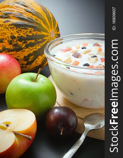 Glass bowl filled with yogurt mixed with fruit pieces arranged with spoon and some fruits around