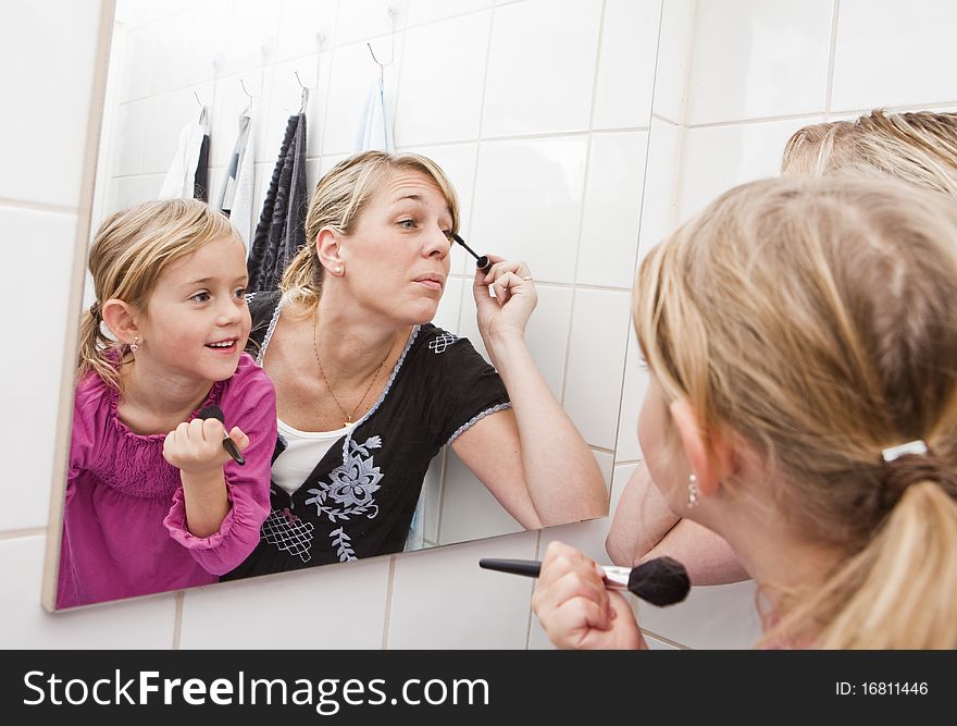 Mother and daughter put on make-up in the bathroom