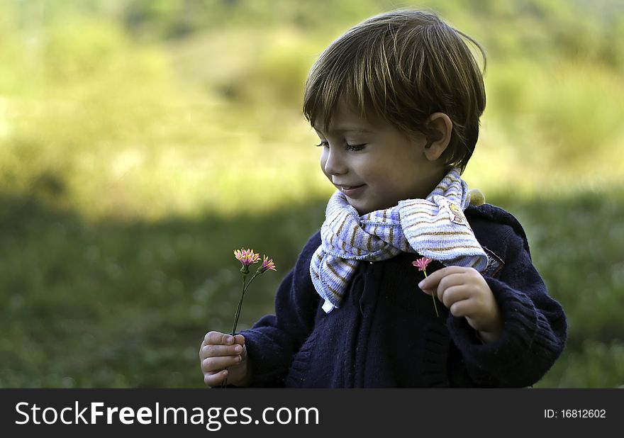 Attractive little blonde boy is holding wildflowers and wearing a scarf. Attractive little blonde boy is holding wildflowers and wearing a scarf