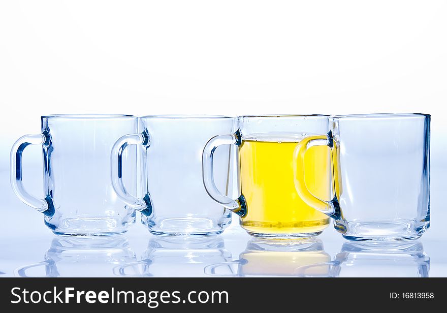 Four glass cups three of which are empty and one with a yellow tea