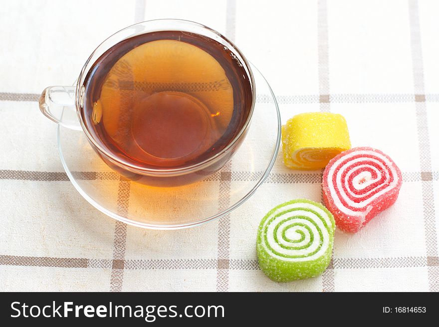 Colored jelly and mug with tea on checkered tablecloth