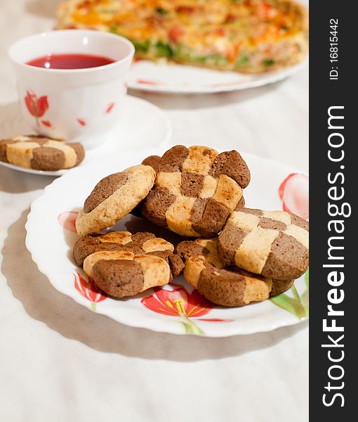 Assorted cookies in white plate and white mug of tea on white table. Assorted cookies in white plate and white mug of tea on white table