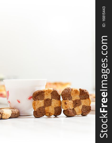 Assorted cookies in white plate and white mug of tea on white table. Assorted cookies in white plate and white mug of tea on white table