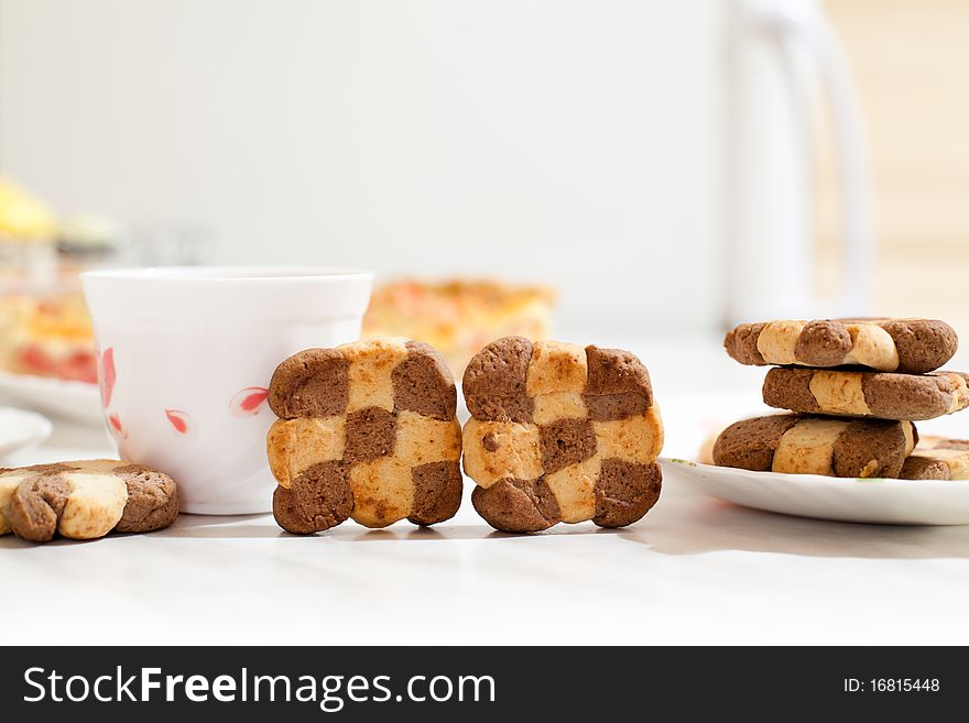 Assorted cookies in white plate and white mug of tea on white table. Assorted cookies in white plate and white mug of tea on white table