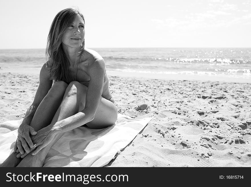 Female in 30's sitting on towel at beach looking away from camera.Black and White image. Female in 30's sitting on towel at beach looking away from camera.Black and White image