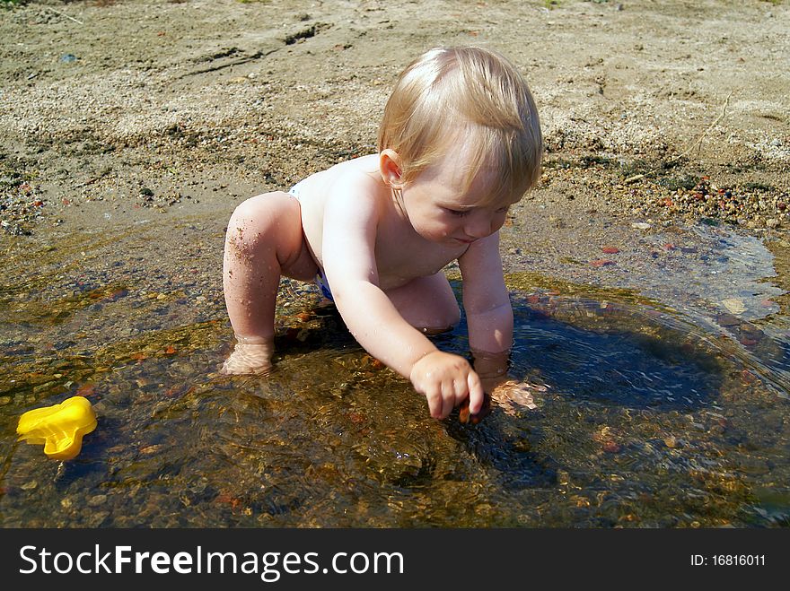 The little boy sits in lake in the summer and plays stones. The little boy sits in lake in the summer and plays stones