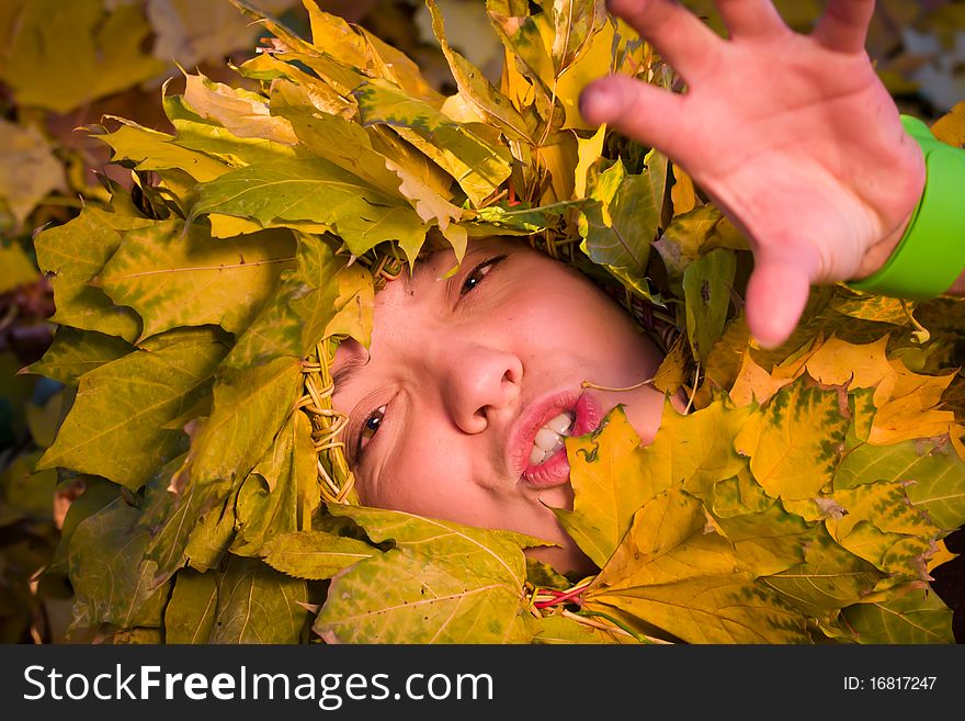 Young smiling woman covered by autumnal leaves