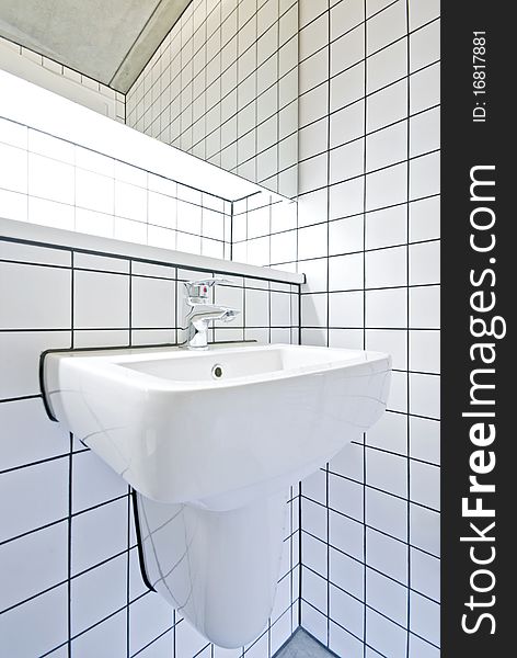 Detail of a contemporary bathroom with white ceramic hand was basin, large mirror and retro white tiled walls situated in a warehouse conversion building. Detail of a contemporary bathroom with white ceramic hand was basin, large mirror and retro white tiled walls situated in a warehouse conversion building