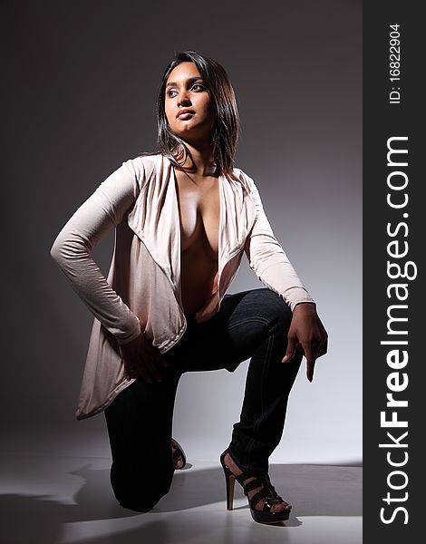 Beautiful and voluptuous young fashion model in a kneeling pose, head turned away. Wearing high heels, blue jeans and open front long sleeve shirt top. Beautiful and voluptuous young fashion model in a kneeling pose, head turned away. Wearing high heels, blue jeans and open front long sleeve shirt top.