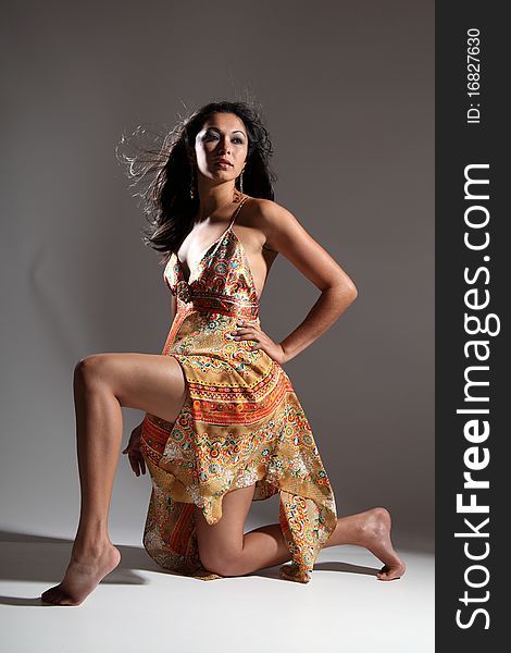 young fashion model girl with long legs kneeling. Head lifted up in dramatic pose, wearing gold pattern sun dress. young fashion model girl with long legs kneeling. Head lifted up in dramatic pose, wearing gold pattern sun dress.