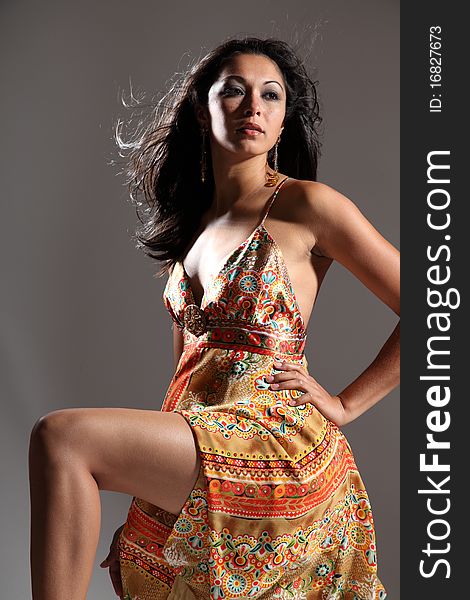 young fashion model girl with long legs kneeling and wearing gold pattern sun dress. Head lifted up in dramatic pose looking away. young fashion model girl with long legs kneeling and wearing gold pattern sun dress. Head lifted up in dramatic pose looking away.