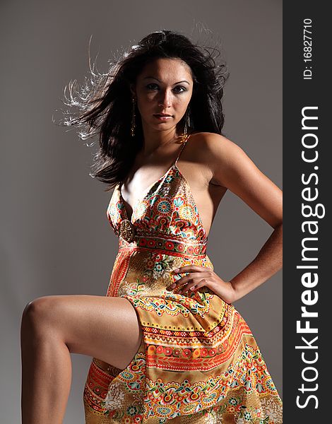 young fashion model girl with long legs and one knee raised wearing gold pattern sun dress. Gazing straight into camera with sultry stare. young fashion model girl with long legs and one knee raised wearing gold pattern sun dress. Gazing straight into camera with sultry stare.