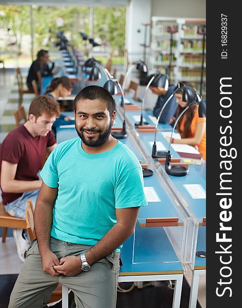 Portrait of male college student sitting on table in library and looking at camera. Vertical shape, high angle view. Portrait of male college student sitting on table in library and looking at camera. Vertical shape, high angle view