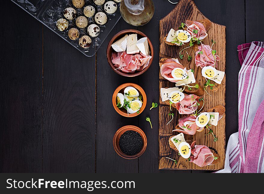 Bruschetta with prosciutto/jamon traditional Italian antipasto. Delicious snack with bread, brie cheese and quails eggs. Health food, tapas. Top view, copy space