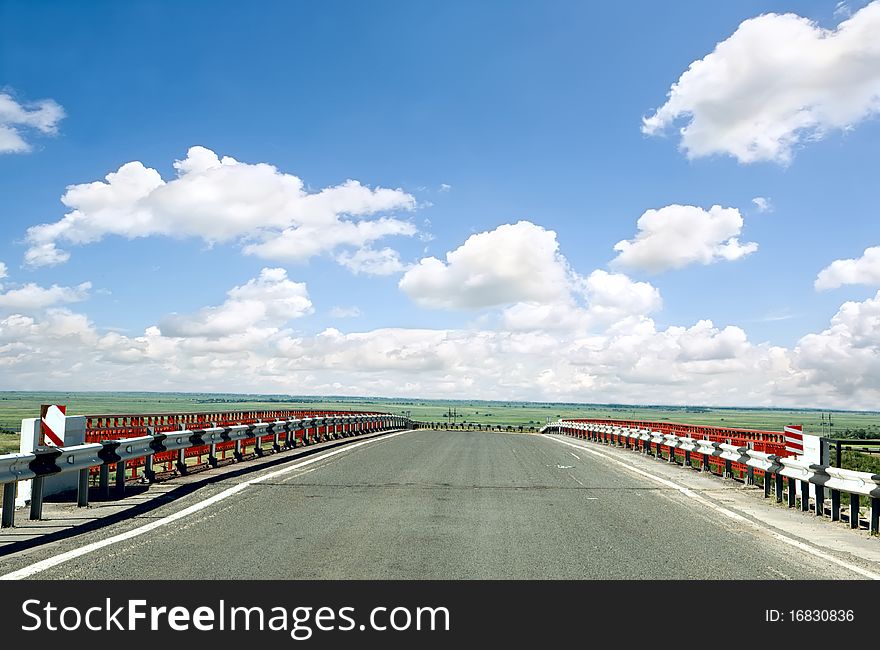 Asphalt road with a fence against the blue sky