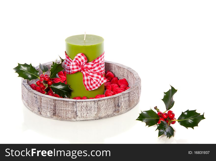 A green candle decorated with stones and holly on a wooden tray isolated over white