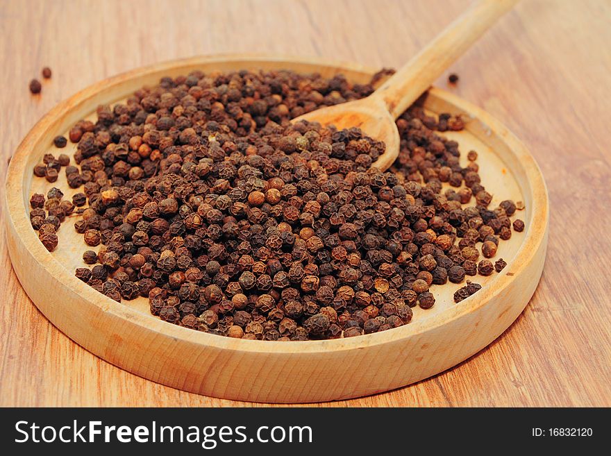 Peppercorns in a wooden bowl with wooden spoon. Peppercorns in a wooden bowl with wooden spoon