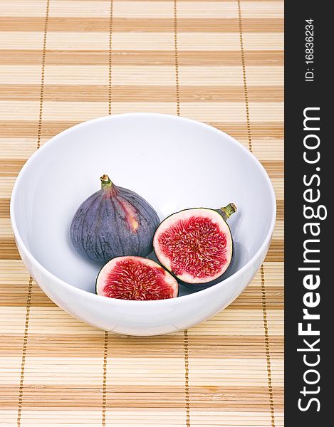 One whole and one sliced fig in a white bowl on bamboo rag. One whole and one sliced fig in a white bowl on bamboo rag