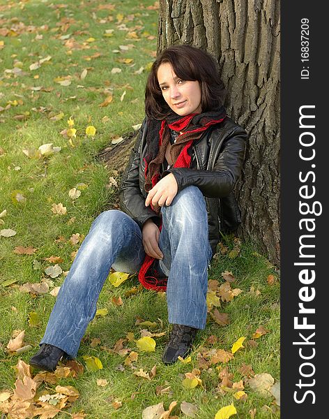 Girl sitting under the tree in an autumn park
