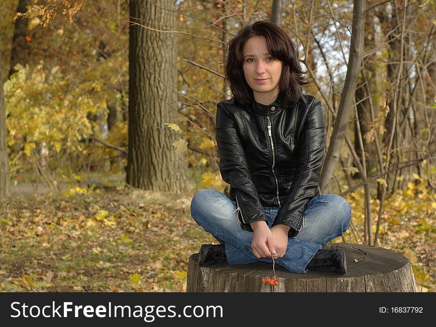 Girl sitting cross-legged on a stump in the autumn forest