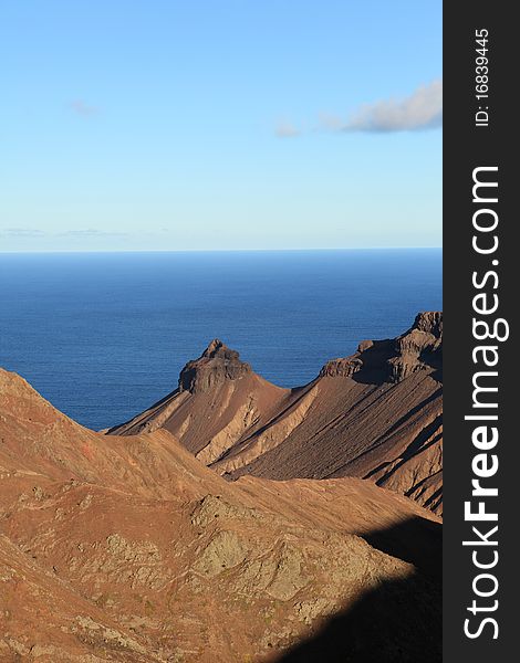 View across the volcanic landscape of St Helena's coastal area in the late afternoon, taken from near Flagstaff looking down to the coastal peak of Turks Cap and the distant South Atlantic Ocean. View across the volcanic landscape of St Helena's coastal area in the late afternoon, taken from near Flagstaff looking down to the coastal peak of Turks Cap and the distant South Atlantic Ocean.