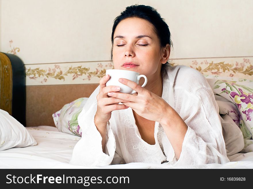 A young woman dreaming and holding white a cup of coffee on bed at bedroom. A young woman dreaming and holding white a cup of coffee on bed at bedroom