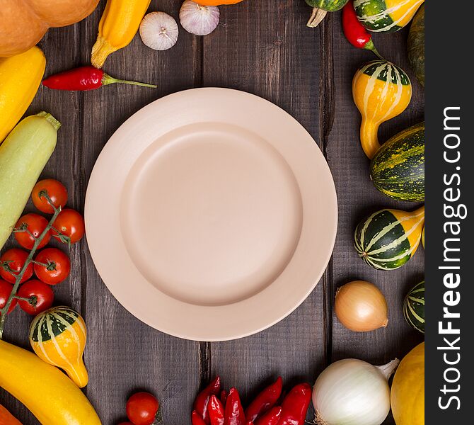Background with empty plate and harvest vegetables around. Wooden board with plate and healthy food. Top view, flat lay, banner for text. Plate with nothing, different vegetables near