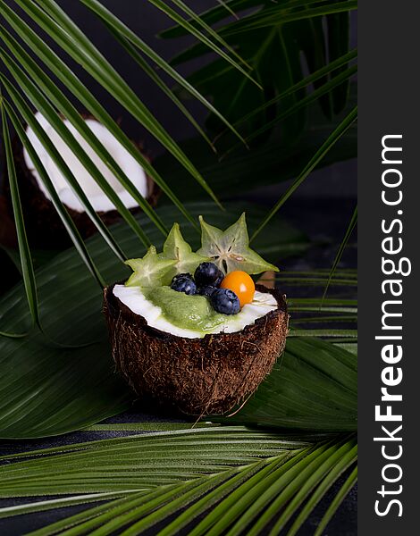 Smoothie in coconut with berries and leaves on background. Concept of tasty tropical food. Copy space for text, banner and blank