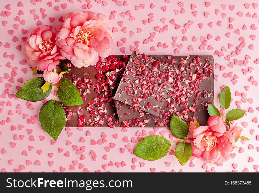 Chocolate with Pieces of Dried Strawberries Lies Stack on Pink Table with Flower