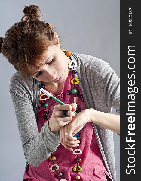 Young girl with pigtails, and colorful necklace laying and writes with a pen on her hand