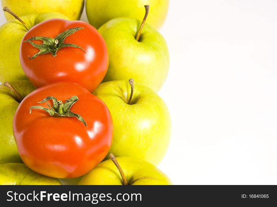 Two rows of green apples are placed vertically on the left of the image. on top of them are two red tomatoes. Two rows of green apples are placed vertically on the left of the image. on top of them are two red tomatoes