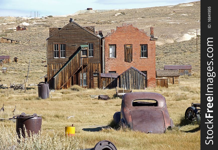 Remains of two houses in Bodie ghost town in California with rusty car in foreground