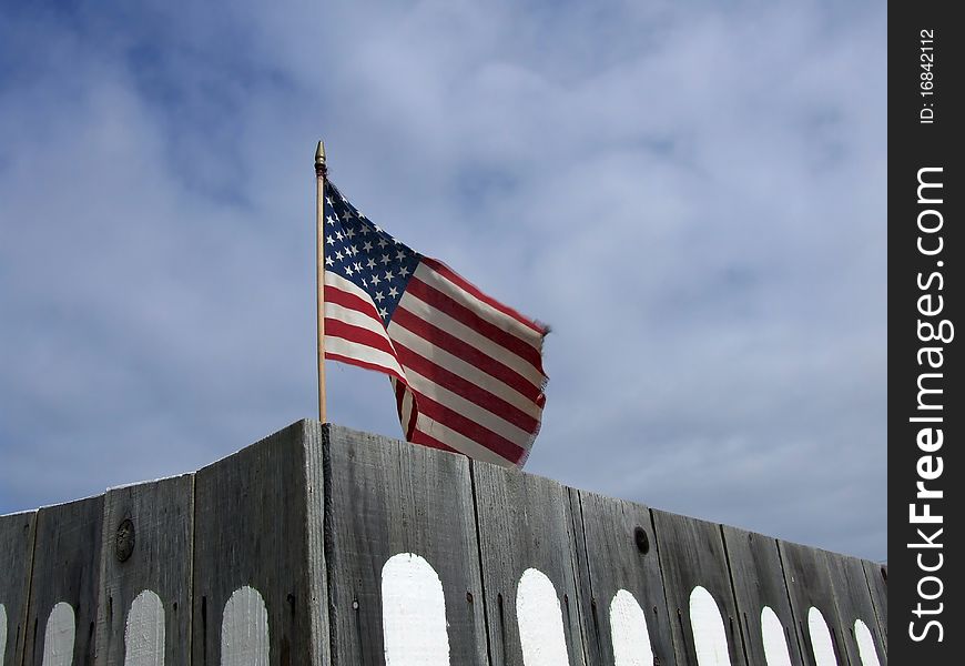 US flag against cloudy sky behind a wooden fence in California, US. US flag against cloudy sky behind a wooden fence in California, US
