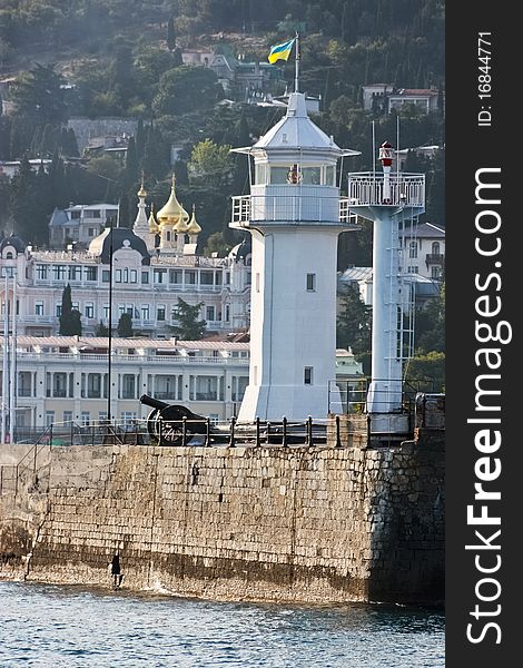 Coastal beacon with an artillery gun on the stone basis at the sea, on a back background of a building, gold domes of church. Coastal beacon with an artillery gun on the stone basis at the sea, on a back background of a building, gold domes of church