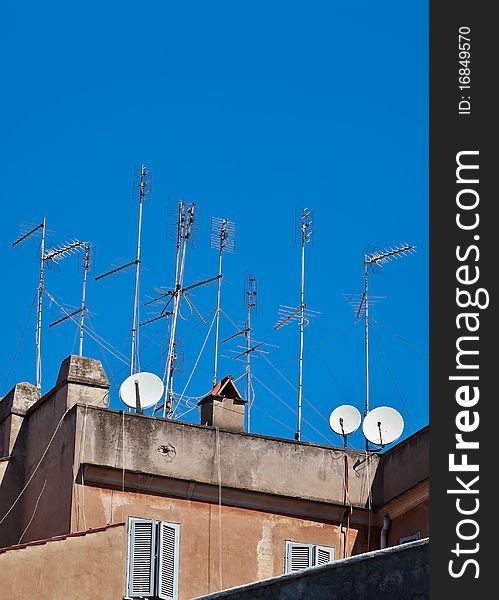 Residential television aerials and satellite dishes on rooftop against clear blue sky.