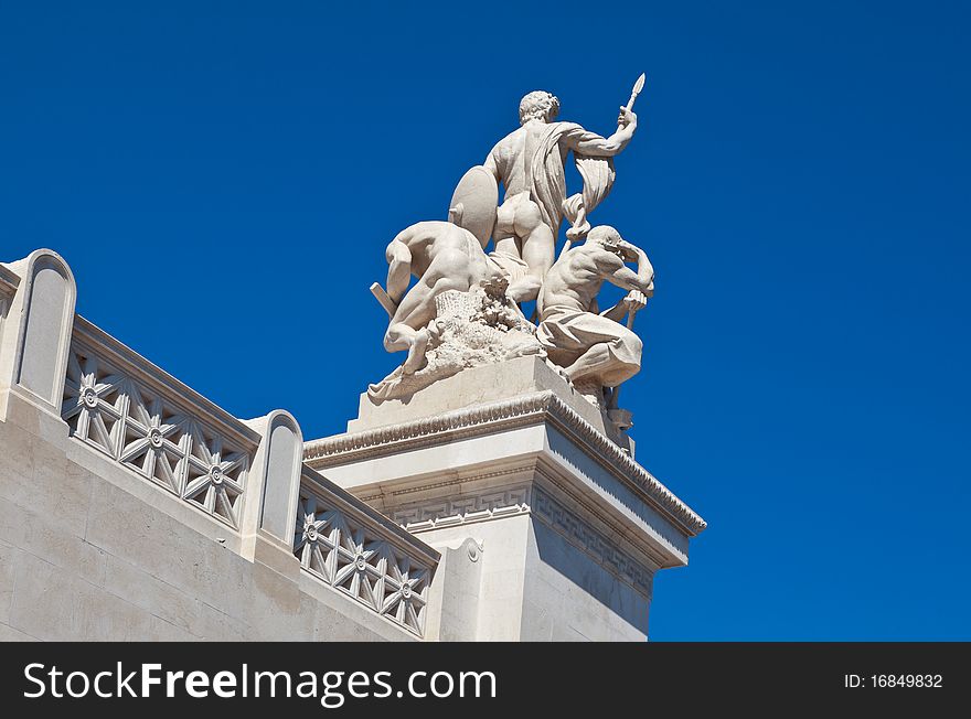 Rear view of marble statue of three Roman men against a clear, blue sky.