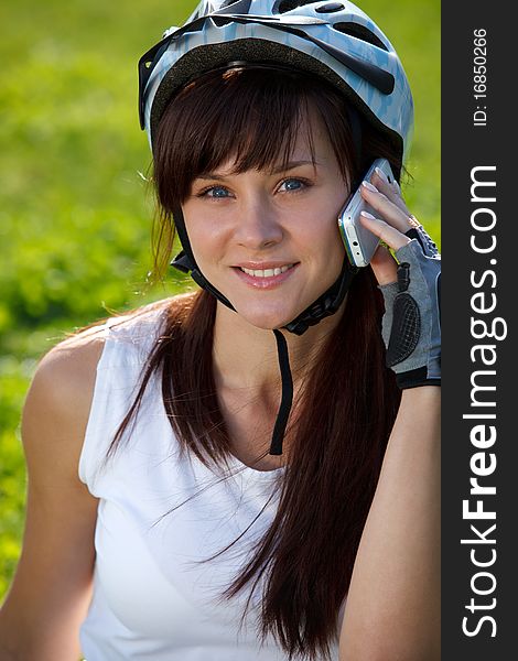 Young female cyclist making a call on the grass background