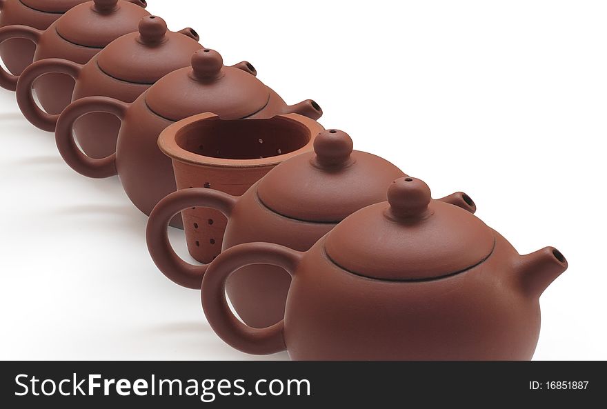 Clay teapots and tea strainer at row on white background