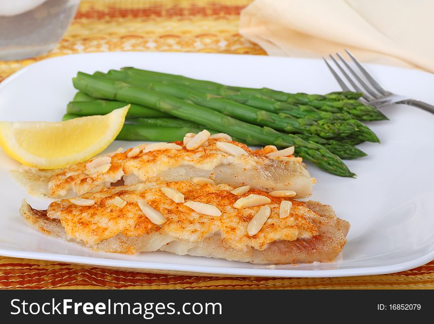 Fish fillets topped with crab meat sauce and almond slivers with asparagus and slice of lemon. Fish fillets topped with crab meat sauce and almond slivers with asparagus and slice of lemon