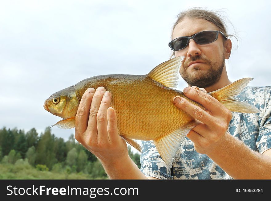 Fisherman holding a rudd fish on the shoreline of a river. Fisherman holding a rudd fish on the shoreline of a river