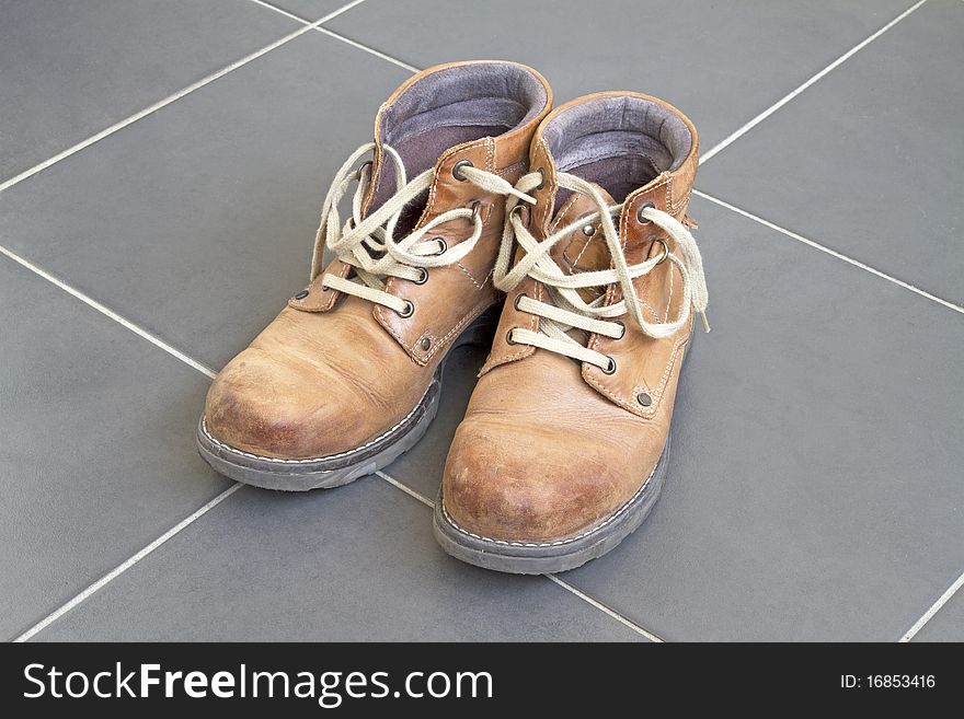 Pair of comfortable old brown boots on grey tiled floor