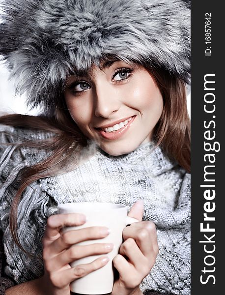 Girl blowing on hot drink dressed in winter clothing