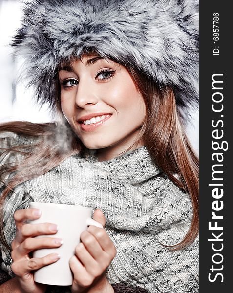 Girl blowing on hot drink dressed in winter clothing