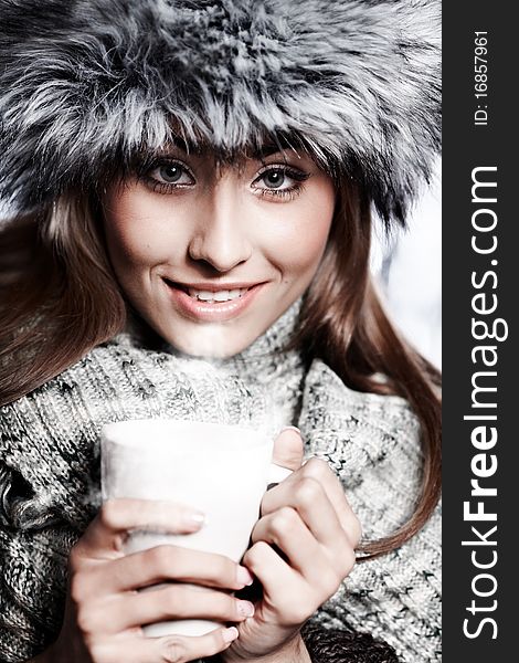 Girl blowing on hot drink dressed in winter clothing