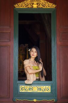 Woman Wearing Thai Costume Combing Hair In Window. Asian Girl Wearing Thai Traditional Dress Hand Holding Hair On Window. Looking Royalty Free Stock Image